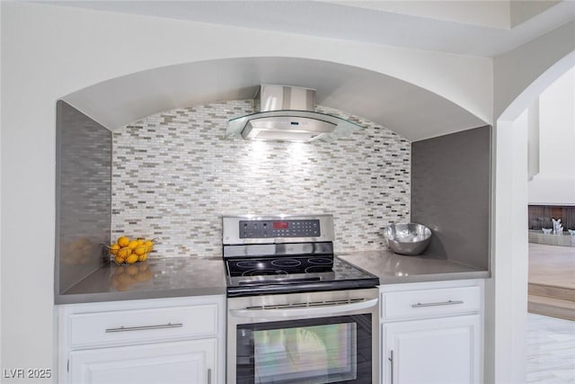 kitchen featuring wall chimney exhaust hood, stainless steel electric range oven, white cabinetry, and tasteful backsplash