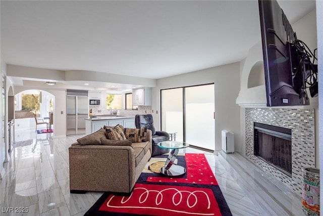 living area with arched walkways and a tiled fireplace