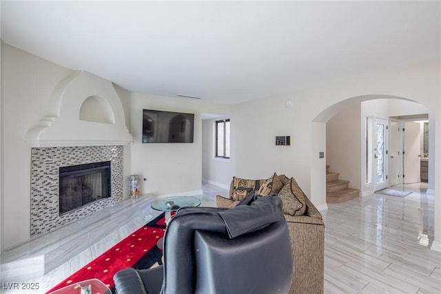 living area featuring baseboards, visible vents, arched walkways, a tiled fireplace, and stairway