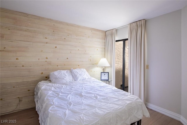 bedroom with wooden walls, baseboards, and wood finished floors