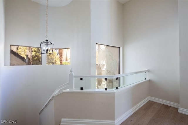 staircase with baseboards, a notable chandelier, a high ceiling, and wood finished floors