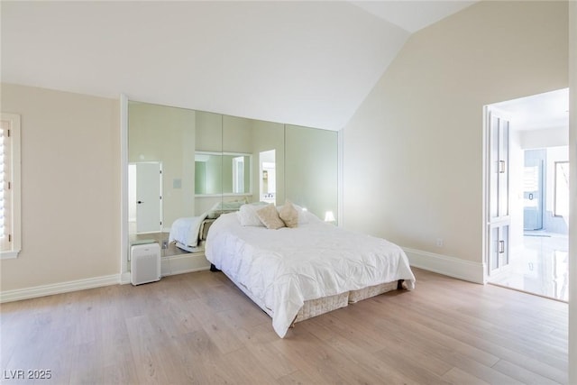 bedroom featuring light wood finished floors, baseboards, high vaulted ceiling, and ensuite bathroom