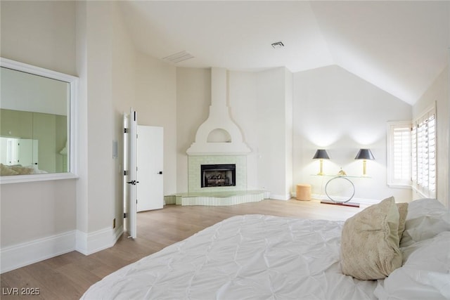 bedroom with baseboards, visible vents, a fireplace with raised hearth, wood finished floors, and high vaulted ceiling