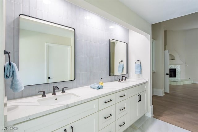 bathroom with double vanity, tile walls, a fireplace with raised hearth, and a sink