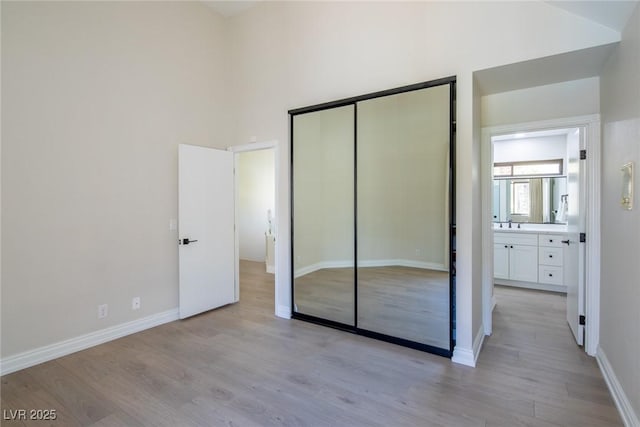 unfurnished bedroom featuring a high ceiling, a closet, baseboards, and light wood finished floors