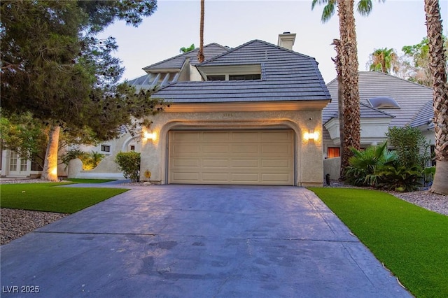 view of front of property featuring driveway, a garage, a chimney, a front lawn, and stucco siding