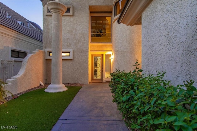 view of exterior entry with fence and stucco siding