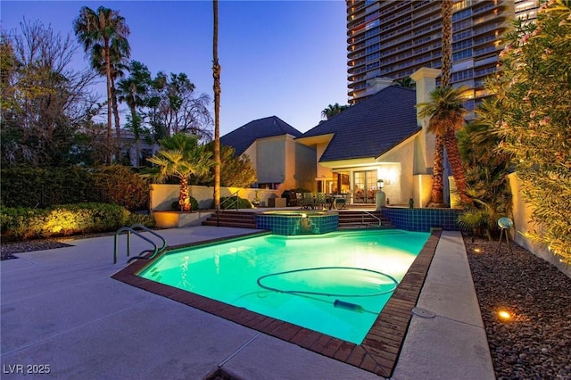 pool at dusk with a pool with connected hot tub, a fenced backyard, and a patio