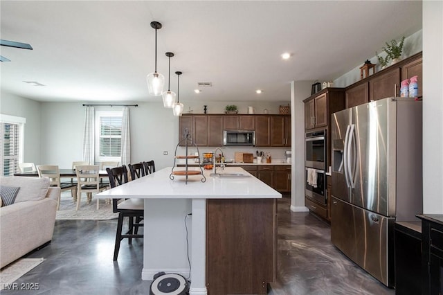 kitchen with appliances with stainless steel finishes, an island with sink, sink, a kitchen breakfast bar, and hanging light fixtures