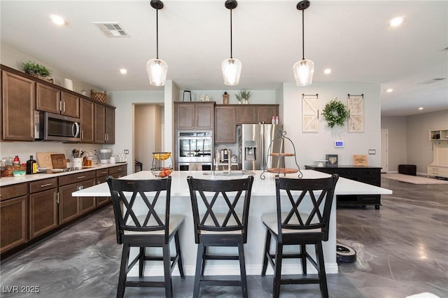 kitchen with appliances with stainless steel finishes, dark brown cabinets, a center island with sink, and decorative light fixtures