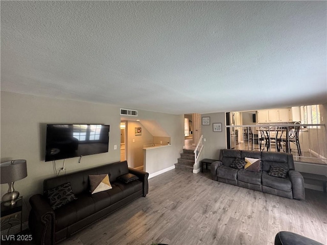 living room with wood finished floors, visible vents, baseboards, a textured ceiling, and stairs