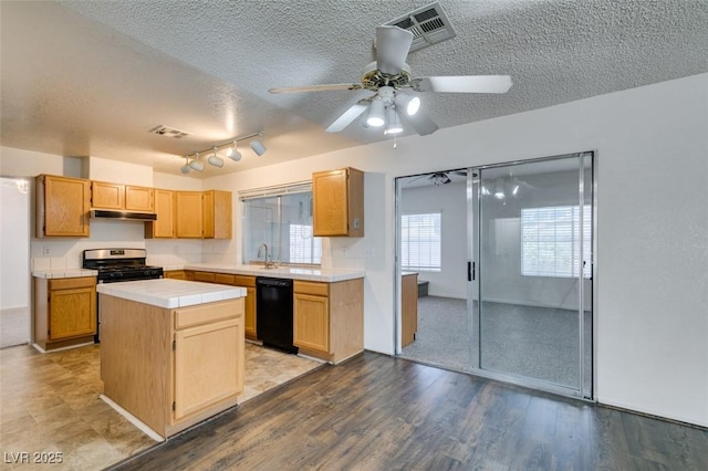 kitchen with stainless steel gas range, a textured ceiling, tile countertops, dishwasher, and a kitchen island