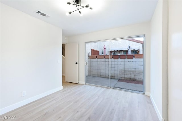 unfurnished room with a notable chandelier and light wood-type flooring