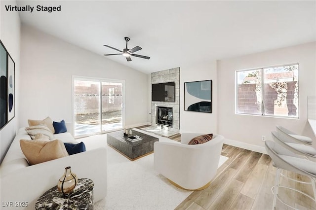 living room featuring a tile fireplace, light hardwood / wood-style floors, a wealth of natural light, and ceiling fan