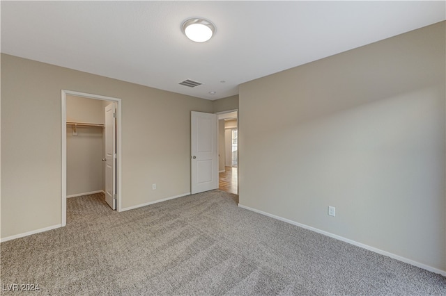 unfurnished bedroom featuring light carpet, a walk in closet, and a closet