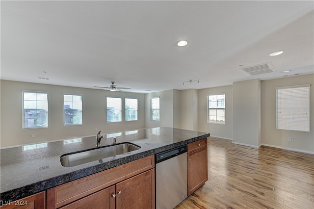 kitchen with a healthy amount of sunlight, stainless steel dishwasher, dark stone counters, and sink