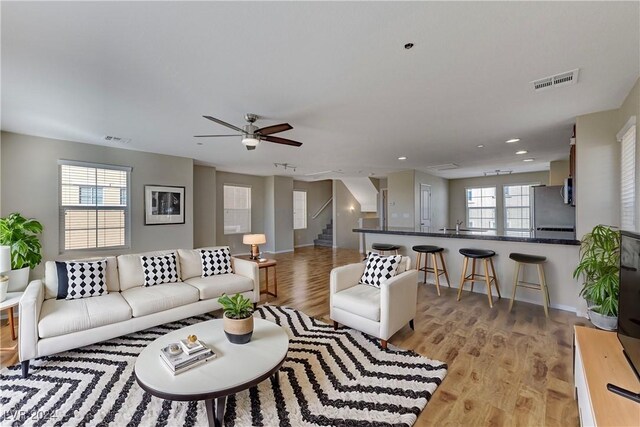 living room featuring light wood-type flooring, ceiling fan, and a healthy amount of sunlight