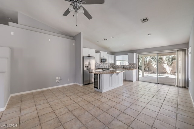 kitchen with decorative backsplash, stainless steel appliances, vaulted ceiling, white cabinetry, and a kitchen island