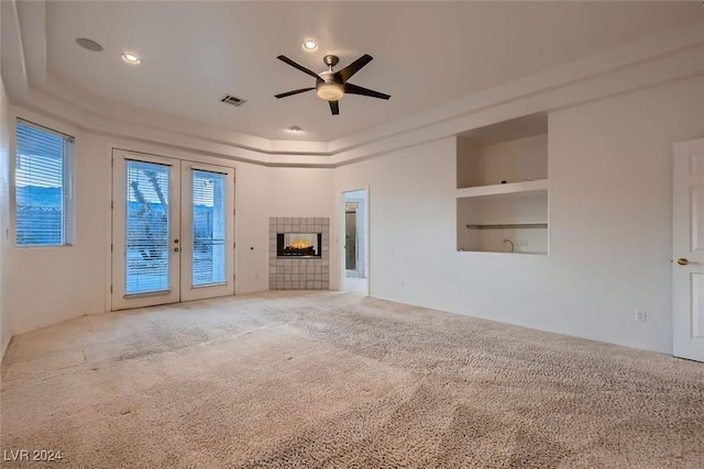 unfurnished living room featuring ceiling fan, french doors, built in features, light colored carpet, and a fireplace