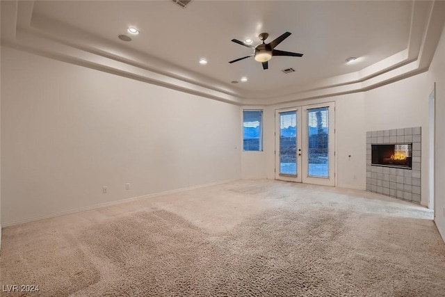 unfurnished living room featuring light carpet, french doors, a raised ceiling, ceiling fan, and a fireplace