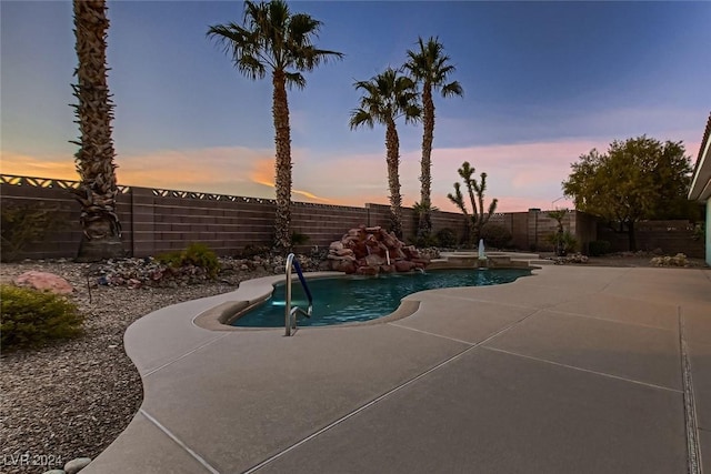 pool at dusk featuring pool water feature and a patio