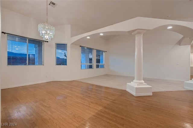 unfurnished living room with decorative columns, a chandelier, and light wood-type flooring