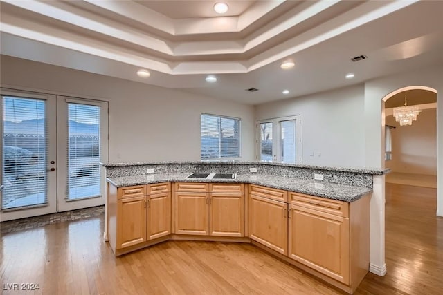 kitchen featuring french doors, light stone counters, a raised ceiling, light hardwood / wood-style flooring, and a notable chandelier