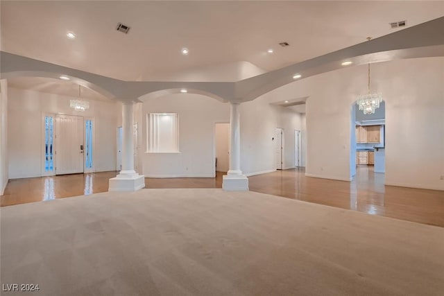 unfurnished living room with a notable chandelier, light wood-type flooring, and ornate columns