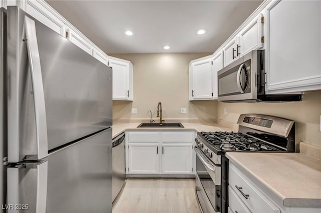 kitchen with stainless steel appliances, sink, white cabinets, and light hardwood / wood-style flooring