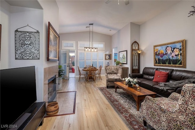 living room with a tile fireplace, an inviting chandelier, vaulted ceiling, and light wood-type flooring