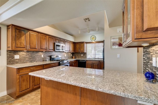 kitchen with rail lighting, light stone countertops, appliances with stainless steel finishes, tasteful backsplash, and kitchen peninsula