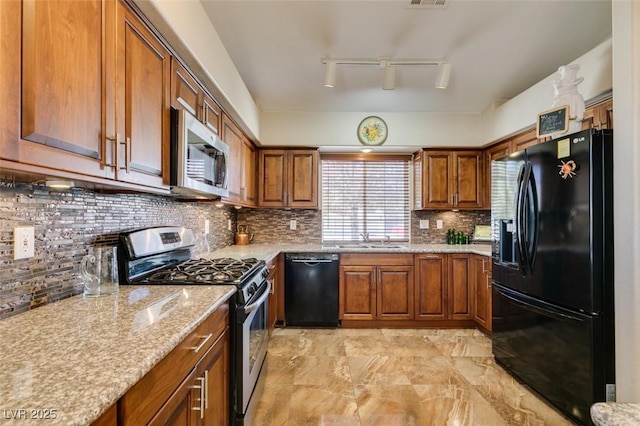 kitchen featuring black appliances, decorative backsplash, light stone counters, and sink