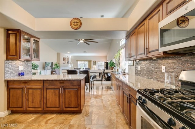 kitchen with light stone countertops, appliances with stainless steel finishes, backsplash, and ceiling fan