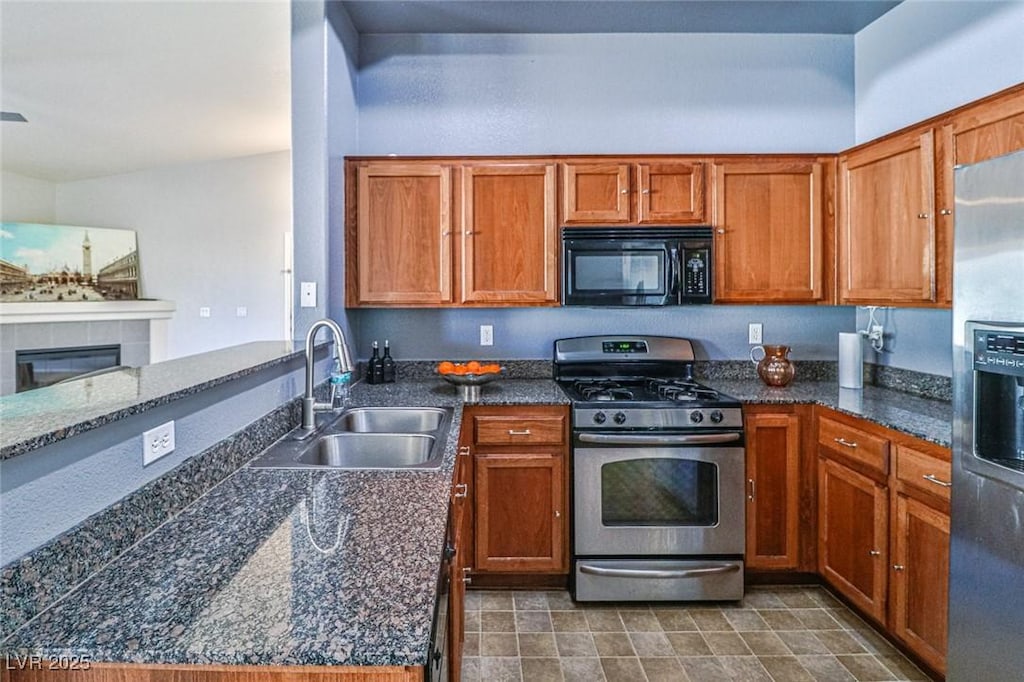 kitchen featuring dark stone countertops, a tile fireplace, sink, and appliances with stainless steel finishes