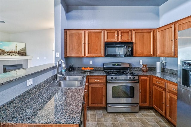 kitchen featuring dark stone countertops, a tile fireplace, sink, and appliances with stainless steel finishes