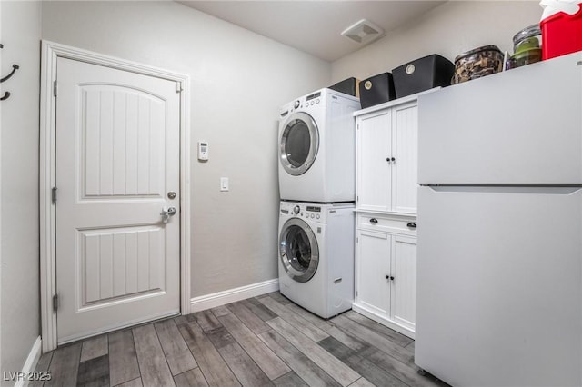 laundry room featuring cabinets, light wood-type flooring, and stacked washing maching and dryer