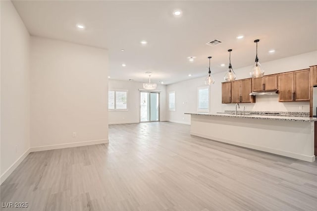 kitchen with light stone countertops, light hardwood / wood-style flooring, pendant lighting, and sink