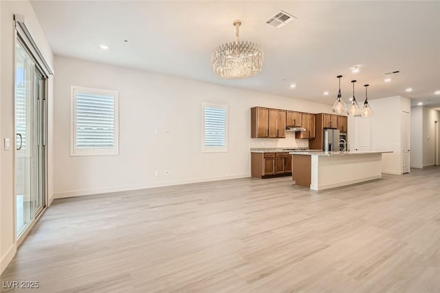 kitchen featuring stainless steel fridge, pendant lighting, light wood-type flooring, and a center island with sink