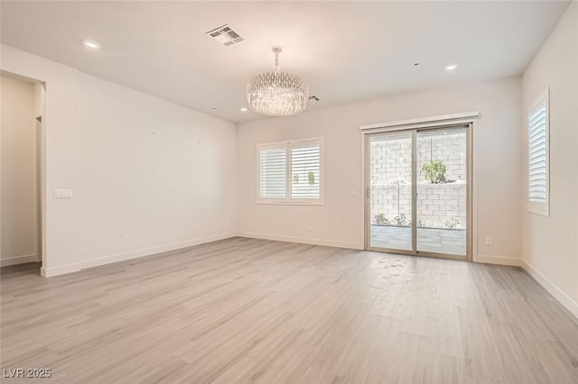 spare room featuring light wood-type flooring and an inviting chandelier