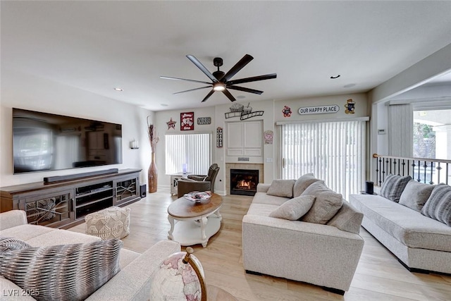 living room featuring ceiling fan, light hardwood / wood-style floors, and a tile fireplace