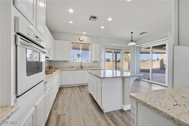 kitchen with white oven, sink, a center island, white cabinetry, and hanging light fixtures