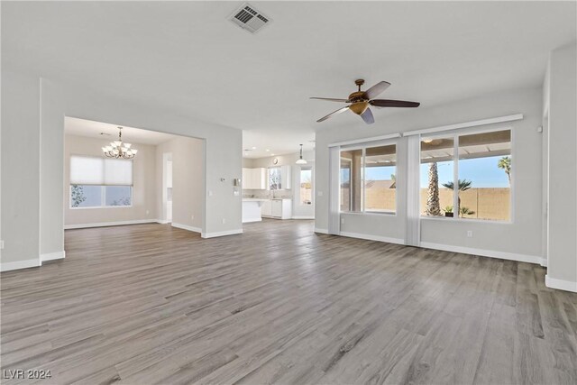 unfurnished living room featuring ceiling fan with notable chandelier, hardwood / wood-style flooring, and plenty of natural light