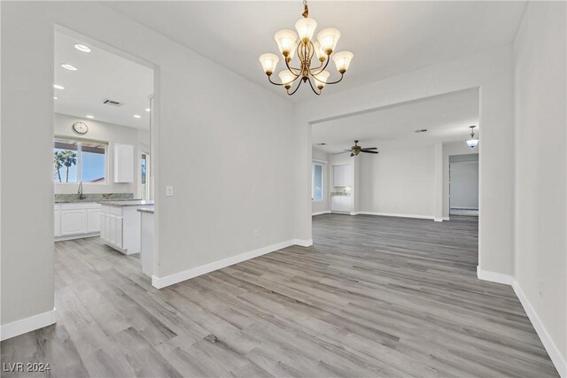 unfurnished dining area with ceiling fan with notable chandelier, sink, and light hardwood / wood-style flooring