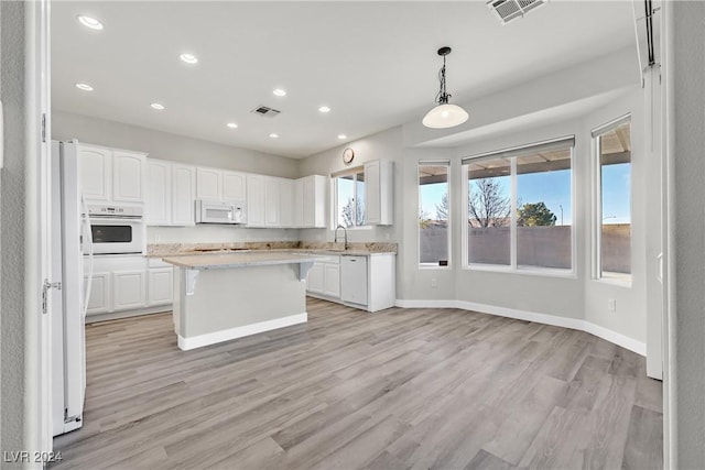 kitchen featuring white cabinetry, a center island, light hardwood / wood-style flooring, pendant lighting, and white appliances