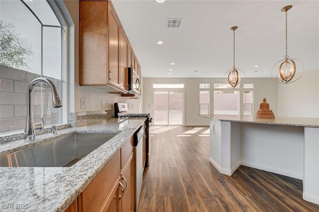 kitchen with sink, light stone countertops, decorative light fixtures, dark hardwood / wood-style flooring, and stainless steel appliances