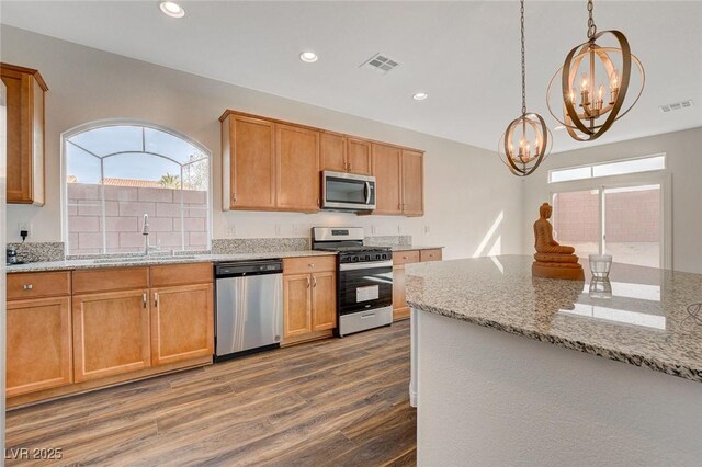 kitchen featuring light stone counters, stainless steel appliances, dark wood-type flooring, pendant lighting, and a notable chandelier