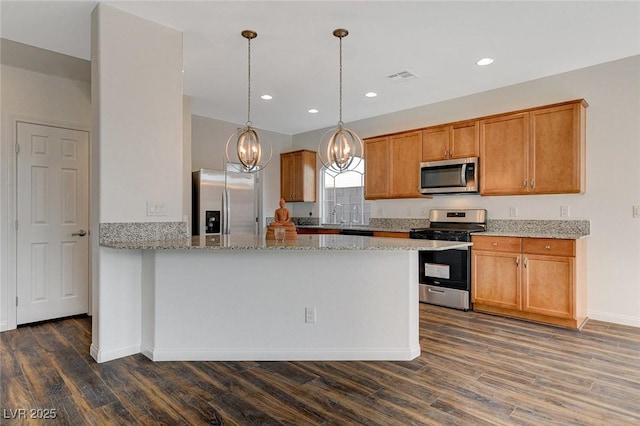 kitchen featuring pendant lighting, dark hardwood / wood-style flooring, light stone counters, and appliances with stainless steel finishes