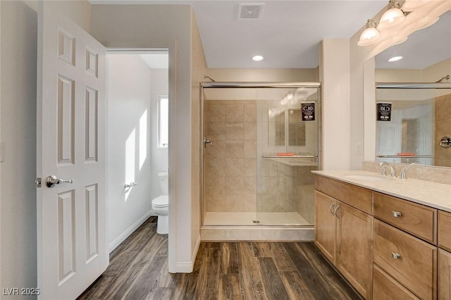 bathroom with wood-type flooring, vanity, toilet, and a shower with shower door