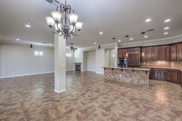 kitchen with a kitchen island with sink, ceiling fan with notable chandelier, hanging light fixtures, ornamental molding, and dark brown cabinets