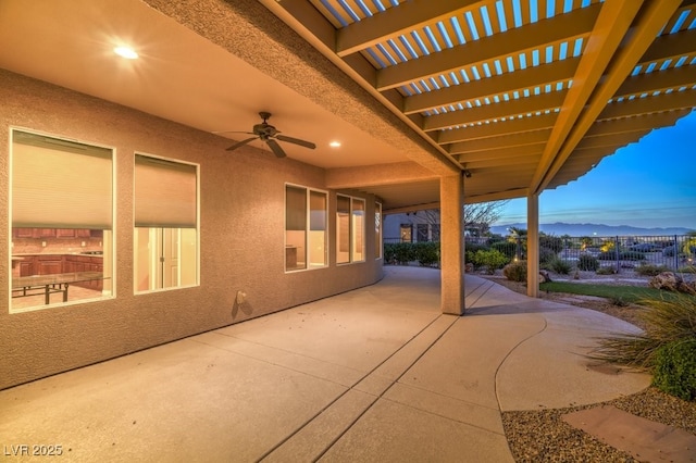 patio terrace at dusk with a mountain view, a pergola, and ceiling fan